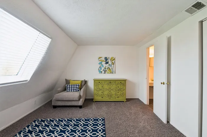 Bright room with modern decor, featuring a cozy armchair, stylish patterned rug, and vibrant art piece on the wall.