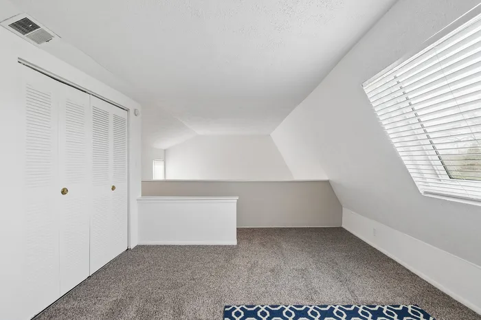 Bright loft-style room with plush carpet and large windows offering abundant natural light.