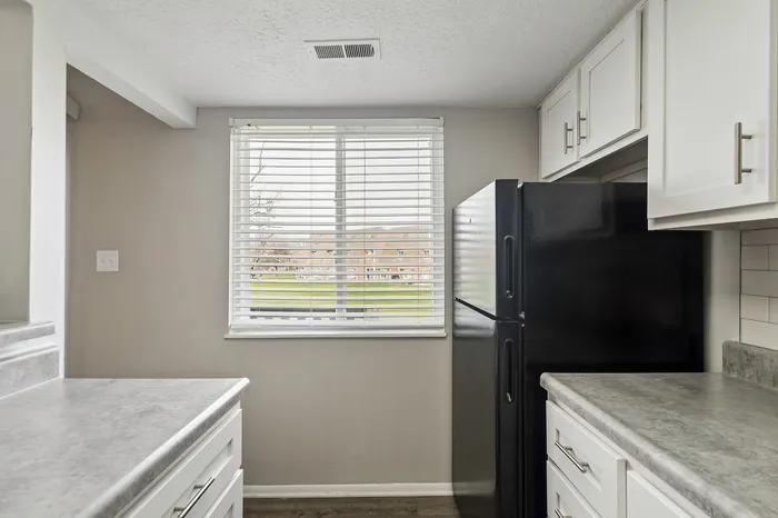 Bright and stylish kitchen featuring modern white cabinets, sleek countertops, and a large window with a view of lush greenery.