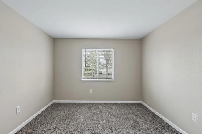 Bright and airy empty room with a large window, offering a peaceful view of trees and a clean, neutral color palette perfect for personalization.