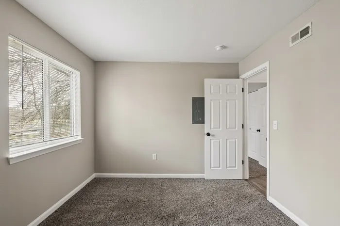 Bright, modern bedroom with plush carpeting and ample natural light from large windows.