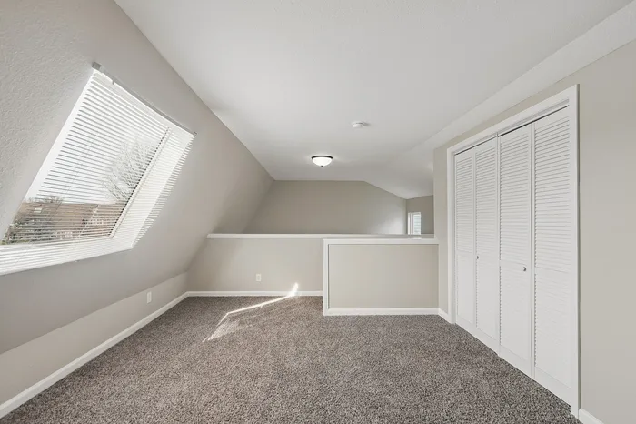 Bright and airy loft space with plush carpeting, large windows, and a modern ceiling light, perfect for relaxation or a home office.