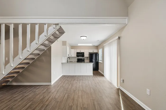 Modern open-plan living area with elegant staircase, featuring bright kitchen with sleek cabinetry and appliances, and large patio doors for natural light.