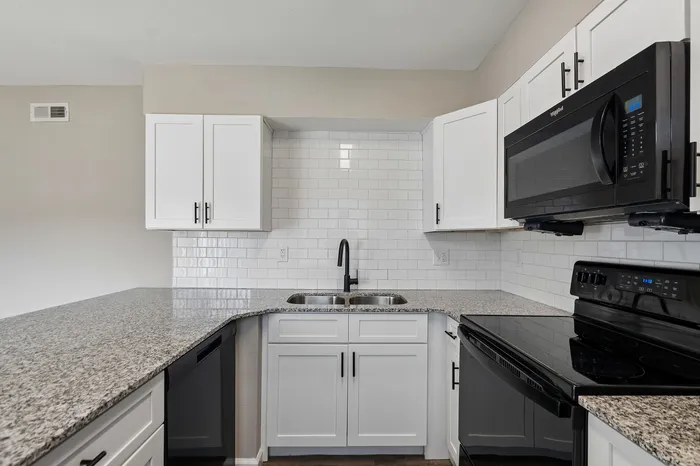 Modern kitchen with sleek granite countertops, white cabinetry, and stainless steel appliances.