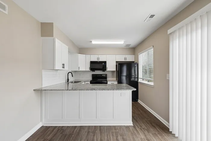 Modern kitchen featuring sleek granite countertops, elegant white cabinetry, and high-end black appliances, offering a bright and inviting space.