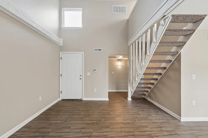 Inviting apartment entryway with elegant wooden flooring and contemporary staircase, offering a touch of sophistication.