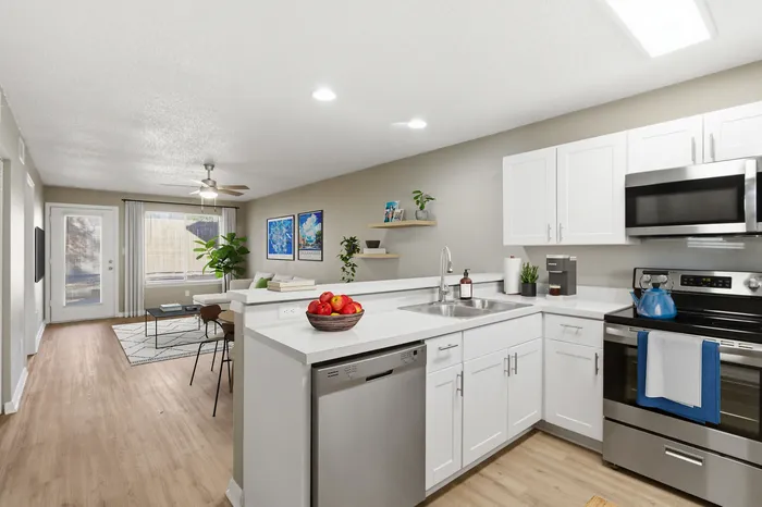 Modern open-concept kitchen and living room with sleek stainless steel appliances, bright white cabinetry, and cozy seating area.