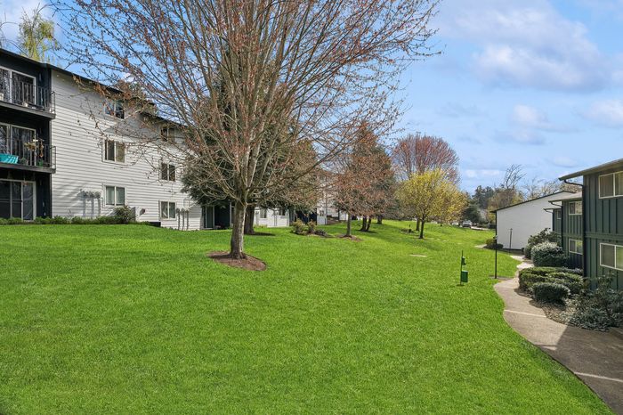 Charming apartment view with lush green lawns, mature trees, and a welcoming pathway showcasing serene outdoor living.