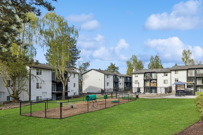 Lush apartment complex with vibrant green landscaping and a fenced recreational area under a clear blue sky.