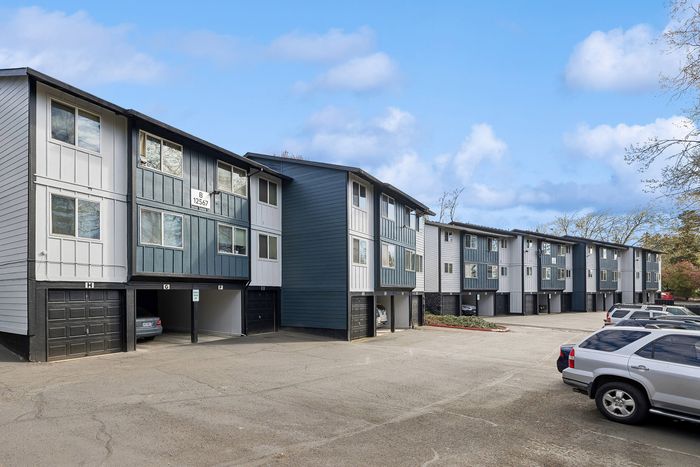 Modern townhouse complex with stylish exteriors, featuring convenient parking and serene surroundings under a clear blue sky.
