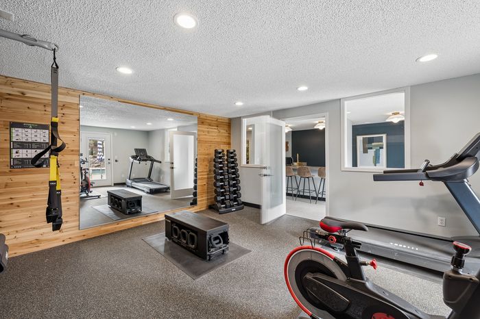 Modern apartment gym with state-of-the-art equipment including a treadmill, stationary bike, and free weights, accented with elegant wood paneling and ambient lighting.