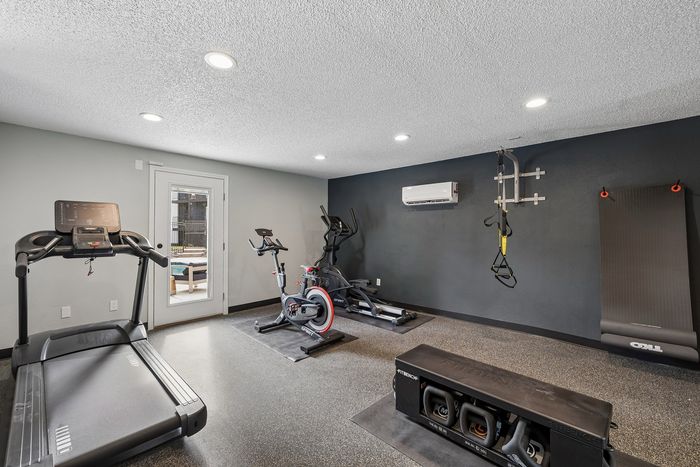 Modern home gym featuring a treadmill, stationary bike, and strength training equipment with pool view through glass door.