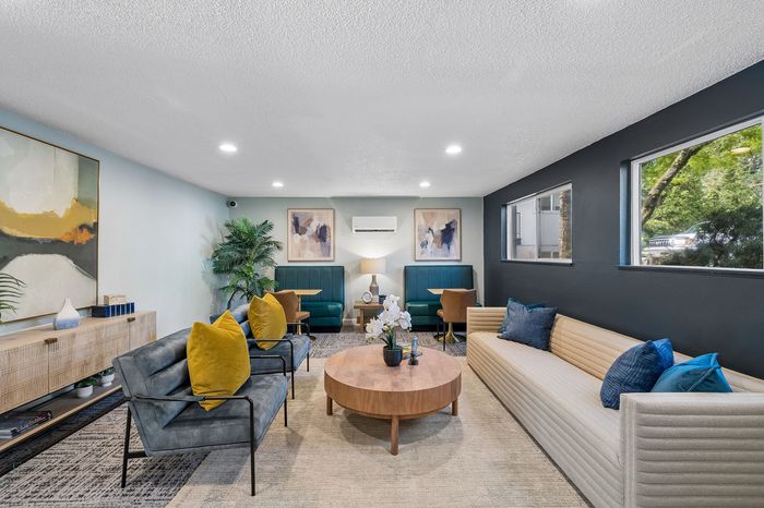 Modern and inviting living area with contemporary decor, featuring chic seating, vibrant artwork, and a sleek coffee table under stylish recessed lighting.