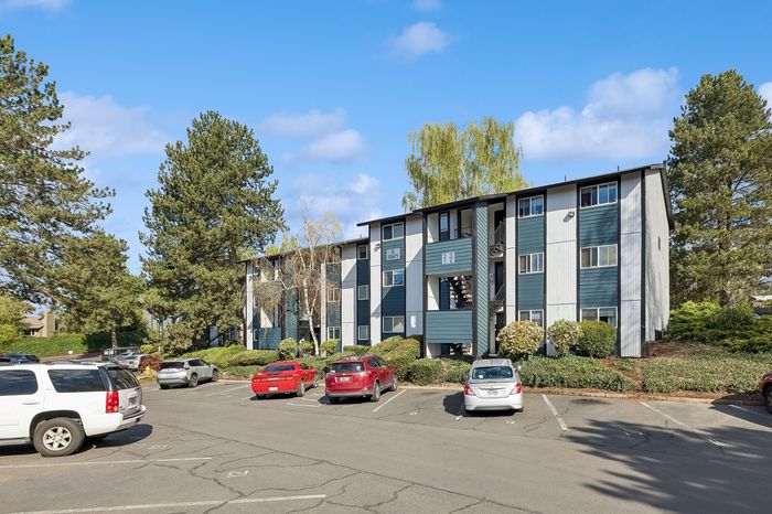 Charming apartment building with modern design surrounded by lush greenery and ample parking.