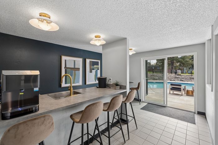 Modern kitchen with chic bar seating and elegant lighting, featuring a stunning pool view through glass doors.