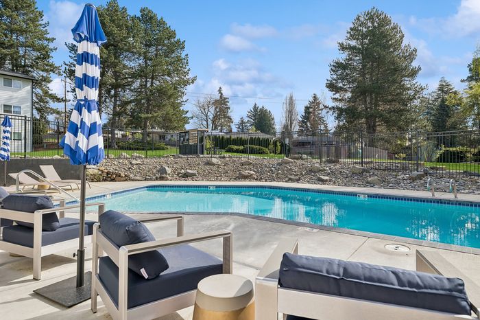 Inviting outdoor pool area featuring stylish loungers and vibrant blue-striped umbrellas, set against a serene natural backdrop.
