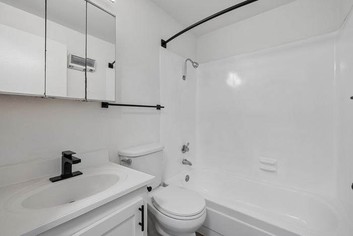 Modern bathroom featuring a sleek white vanity, storage mirror, and pristine bathtub with elegant black fixtures.