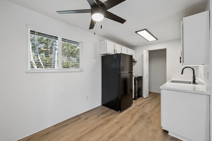 Bright and modern kitchen featuring sleek black appliances, crisp white cabinets, and beautiful hardwood floors under a ceiling fan.