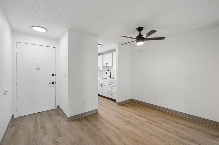 Modern apartment entryway featuring sleek hardwood floors and a ceiling fan, leading into a bright, contemporary kitchen with white cabinetry.