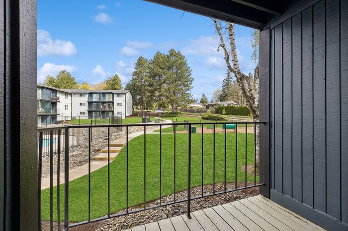 Charming view from a balcony showcasing lush green lawns, modern apartment buildings, and serene outdoor paths.