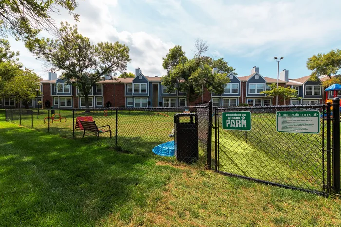 Charming dog park with fenced area and vibrant landscaping set against stylish townhouses, perfect for pet lovers.