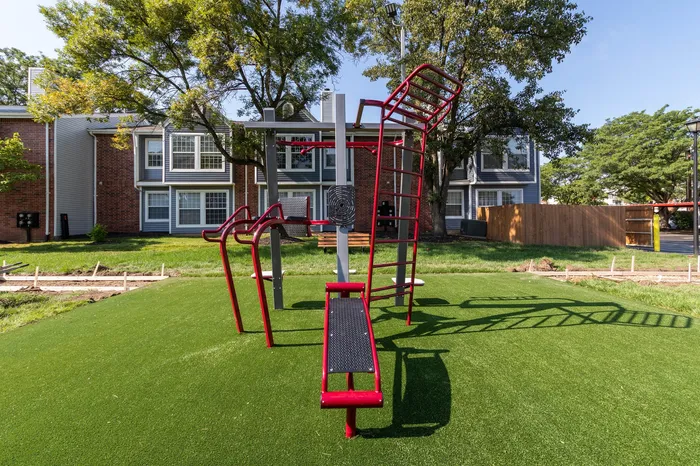 Inviting outdoor playground with vibrant red exercise equipment set against a charming brick apartment complex.