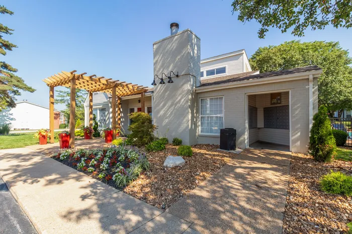 Charming apartment exterior featuring a stylish pergola, vibrant garden, and modern mailbox area, ideal for enjoying serene outdoor living.