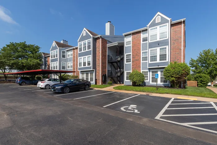 Charming apartment complex with red brick and gray siding, featuring ample parking and a sunny exterior.