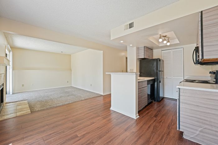 Charming open-concept living area with modern kitchen, wood flooring, and cozy carpeting, perfect for contemporary living.
