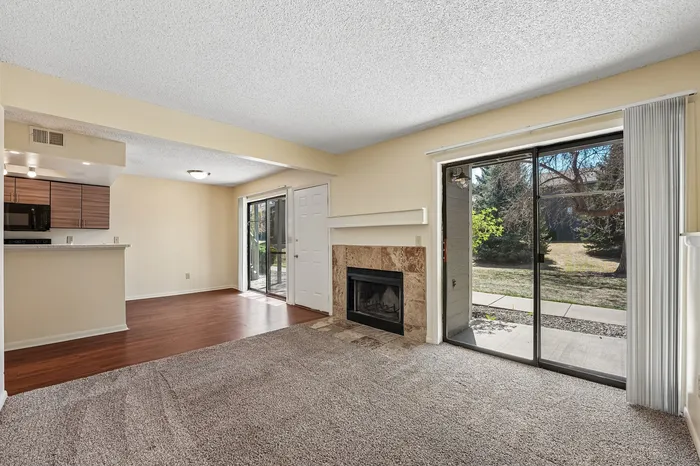 Inviting living room with plush carpet, a cozy fireplace, and large sliding doors leading to a lush outdoor view, adjacent to a modern kitchen.
