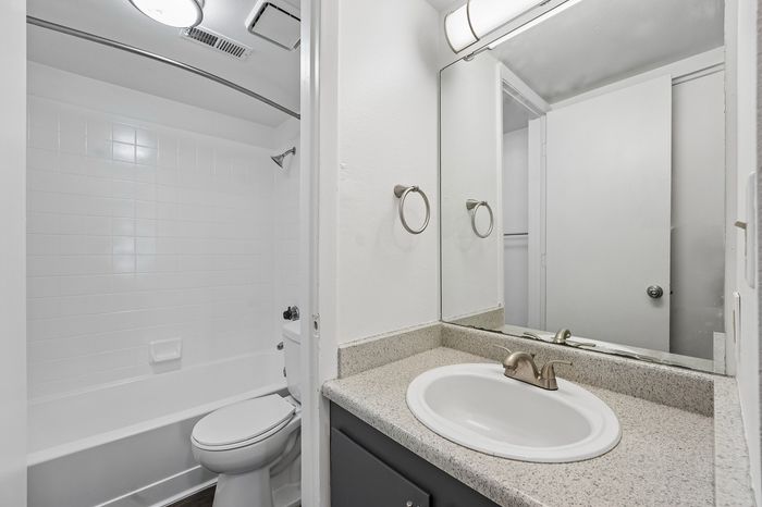 Bright and modern bathroom with sleek quartz countertop, stylish vanity mirror, and pristine white tile bathtub.