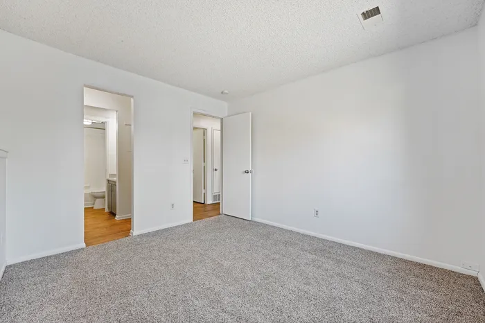Bright and inviting bedroom with plush carpet, showcasing a convenient en-suite bathroom.