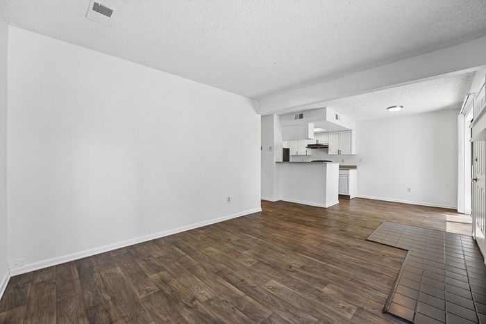 Modern apartment interior with elegant hardwood floors, an open living space, and a bright kitchen featuring sleek cabinetry.