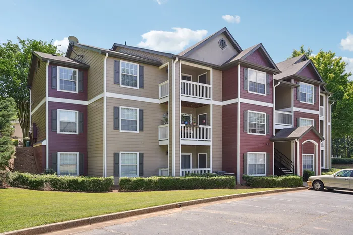 Charming three-story apartment building with stylish balconies, surrounded by lush greenery and ample parking area.