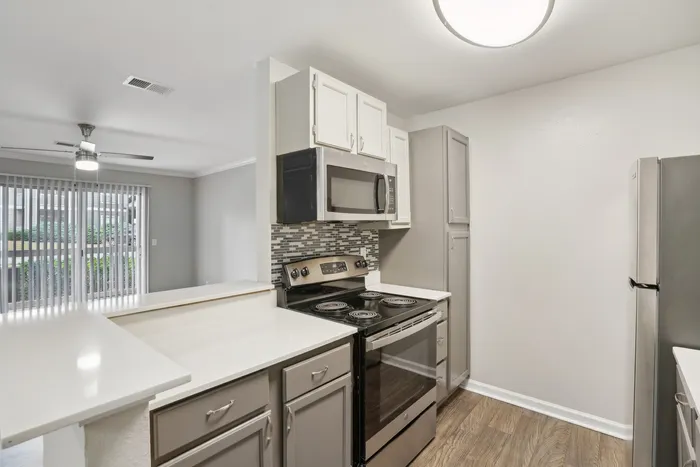 Modern kitchen with sleek stainless steel appliances, stylish tiled backsplash, and open layout leading to a bright living area with large windows.
