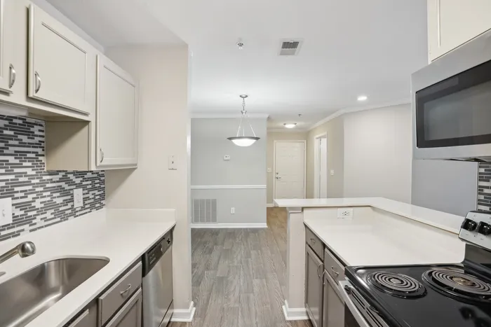 Contemporary kitchen with sleek countertops, stylish backsplash, and modern appliances leading into a spacious hallway.