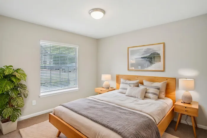 Bright and cozy bedroom featuring a comfortable wooden bed, elegant lighting, and lush green plant accents.