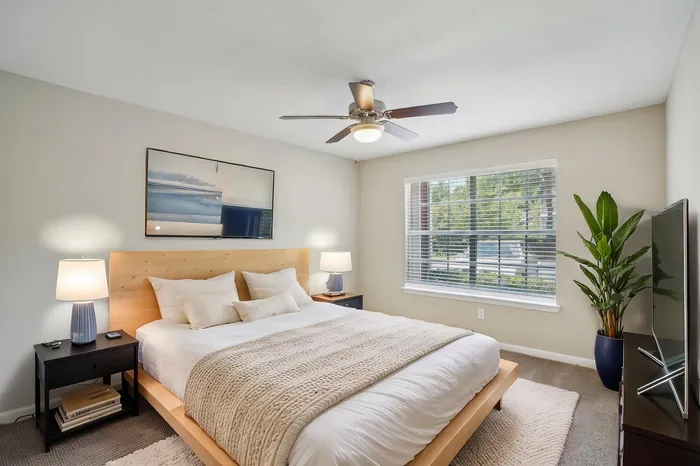 Inviting bedroom with modern decor, featuring a comfortable double bed, stylish ceiling fan, and natural light through large windows.