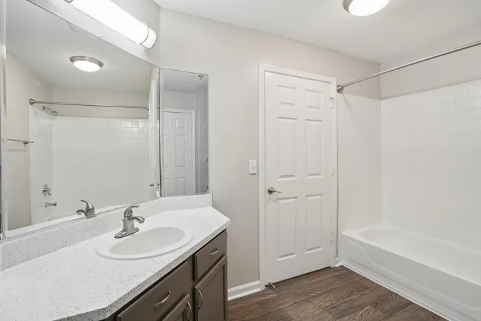 Modern bathroom with sleek white countertop, elegant fixtures, and a pristine bathtub accented by warm wood floors.