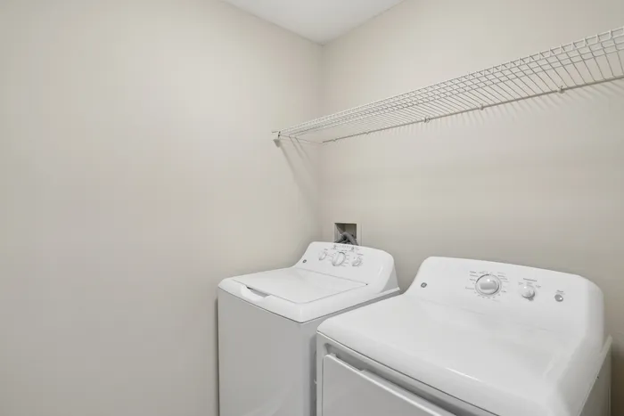 Chic apartment laundry room with modern washer and dryer, featuring a stylish white wire shelf above.