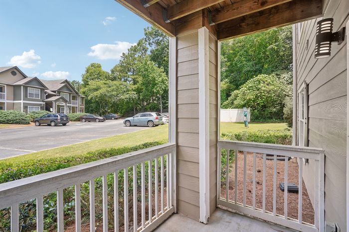 Inviting apartment porch with stylish railing, offering a view of lush greenery and spacious parking area under a clear blue sky.