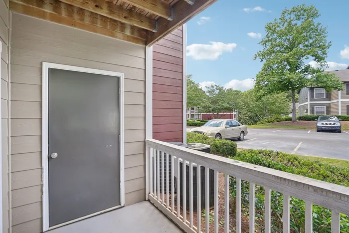 Charming apartment balcony with a view of lush greenery and a well-maintained parking area, offering a peaceful and inviting atmosphere.