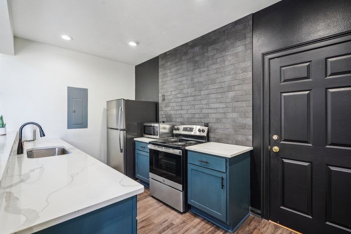 Modern kitchen with sleek marble countertops, stainless steel appliances, and chic blue cabinetry against a stylish dark brick wall.