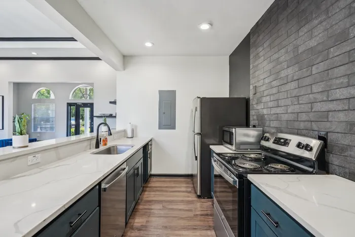 Sleek modern kitchen with stylish white countertops, dark cabinetry, stainless steel appliances, and chic brick accent wall.
