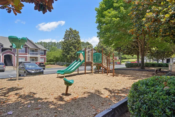 Inviting apartment complex features a charming playground surrounded by lush greenery and comfortable seating.