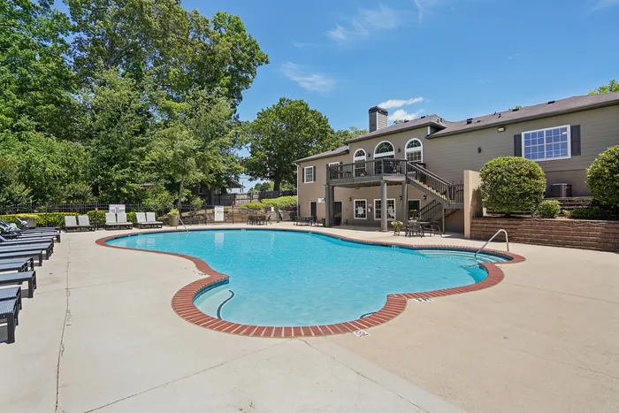 Inviting outdoor pool area with sun loungers, surrounded by lush greenery and a stylish residential building under a blue sky.