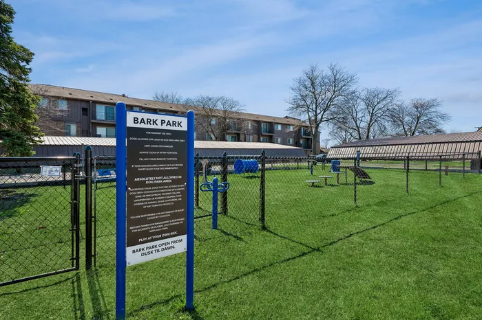 Inviting pet-friendly apartment community showcasing a well-maintained dog park with agility equipment, surrounded by a vibrant green lawn and comfortable outdoor seating.