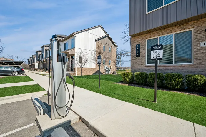 Modern apartment complex with eco-friendly electric vehicle charging stations, well-maintained sidewalks, and lush green landscaping.