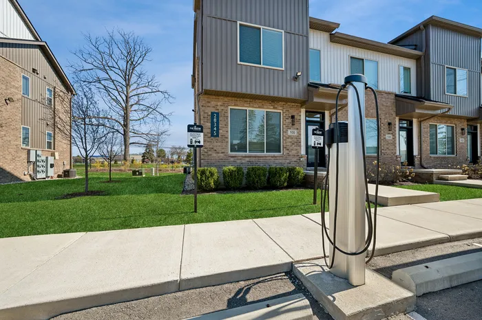 Modern townhouse complex with lush green lawns and electric vehicle charging station, perfect for eco-friendly living.
