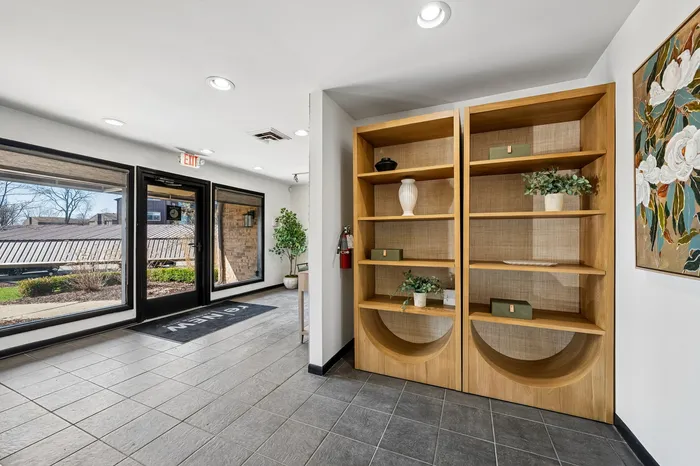Bright apartment lobby with elegant shelving, modern decor, and large windows showcasing a landscaped garden view.